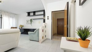 A modern living room with a sofa, a coffee table, and a potted plant. There is a door leading to another room and a wall-mounted shelf with decorative items. - Casa Giovanna by Wonderful Italy (Bari)