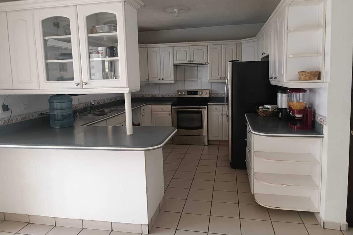 Una cocina con gabinetes blancos, un refrigerador negro, una estufa y un dispensador de agua.