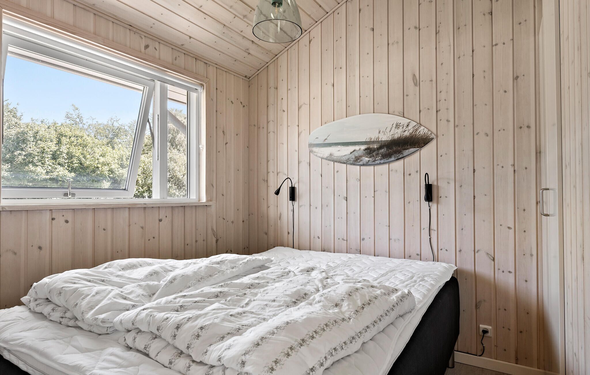 Camera da letto con un letto, una finestra, pareti in legno e un portalampada fissato alla parete.