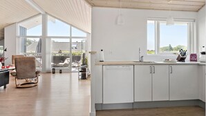 Amplia sala de estar con un ventanal grande, una cocina con alacenas blancas y techo de madera.