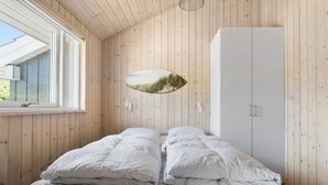 Un dormitorio con pared de paneles de madera, una cama con ropa de cama a rayas, un armario y una lámpara fijada a la pared.