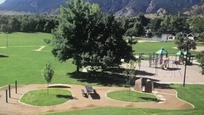Un parque con un área de juegos, zonas de picnic y un árbol grande.