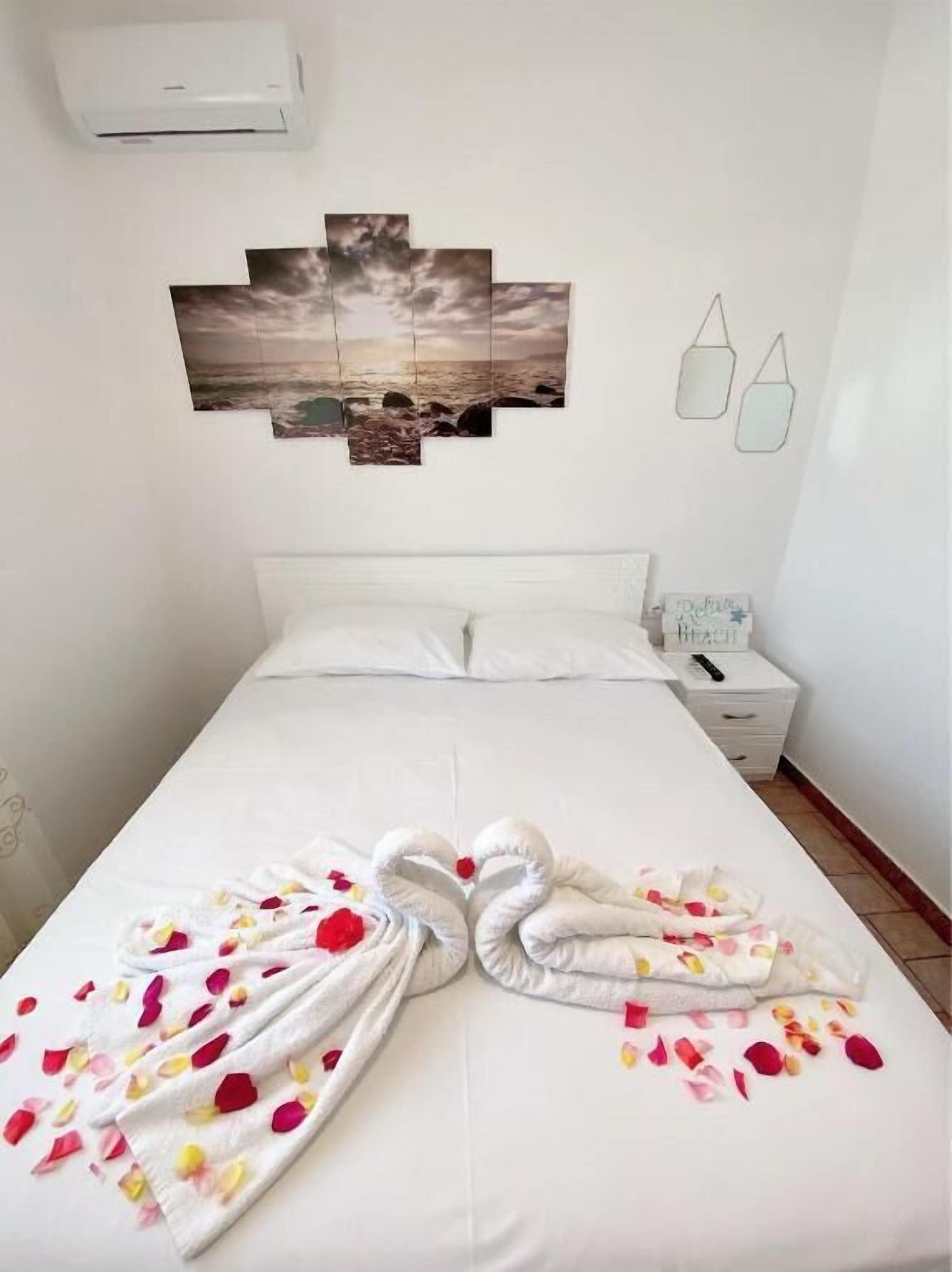 A hotel room with a bed, a nightstand, a wall-mounted air conditioner, and a wall art piece.