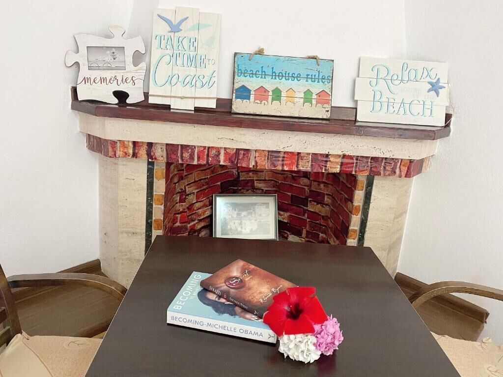 A fireplace mantel with decorative signs, a book titled "Becoming-Michelle Obama," and a vase with flowers.