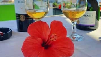 Una mesa con dos copas de vino blanco, una botella de vino y una flor de hibisco rojo.