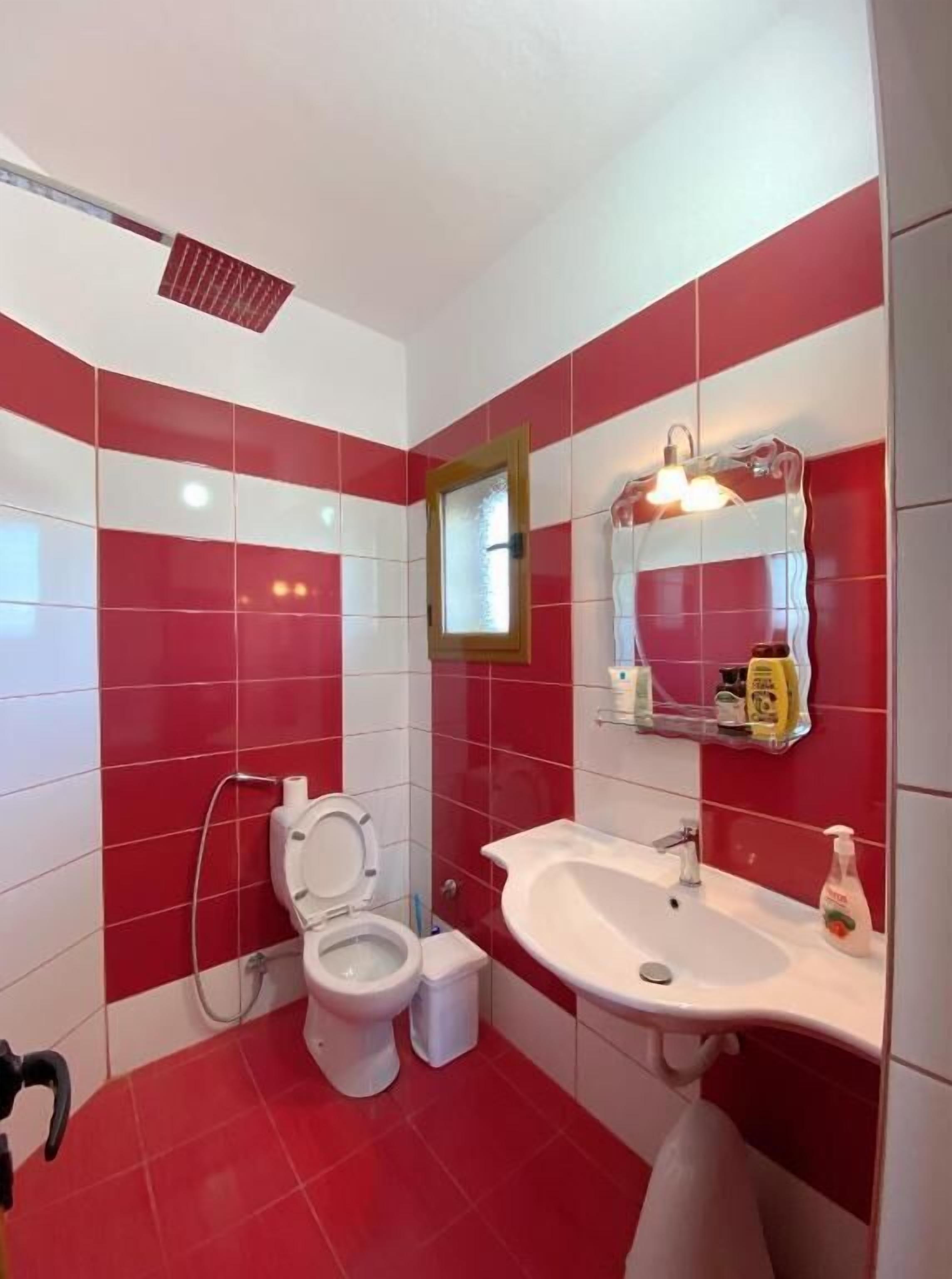 A bathroom with red and white tiles, a white sink, a mirror, and a shower.