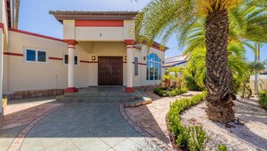 A building with a tiled entrance, a palm tree, and a stone pathway. - Sleeps 11 6 Bedrooms Privatepool Outdoor Dining (Noord)