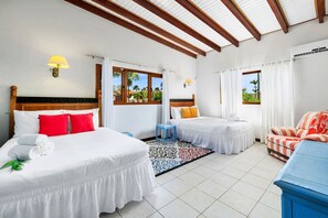 A hotel room with two beds, a blue side table, a patterned rug, and a view of palm trees through the windows. - Spacious 4BR Villa Private Pool Cozy Location (Oranjestad)