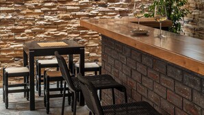 Een rustieke bar met een stenen achtergrondmuur, een houten toog en zitplaatsen met stoelen en een tafel.