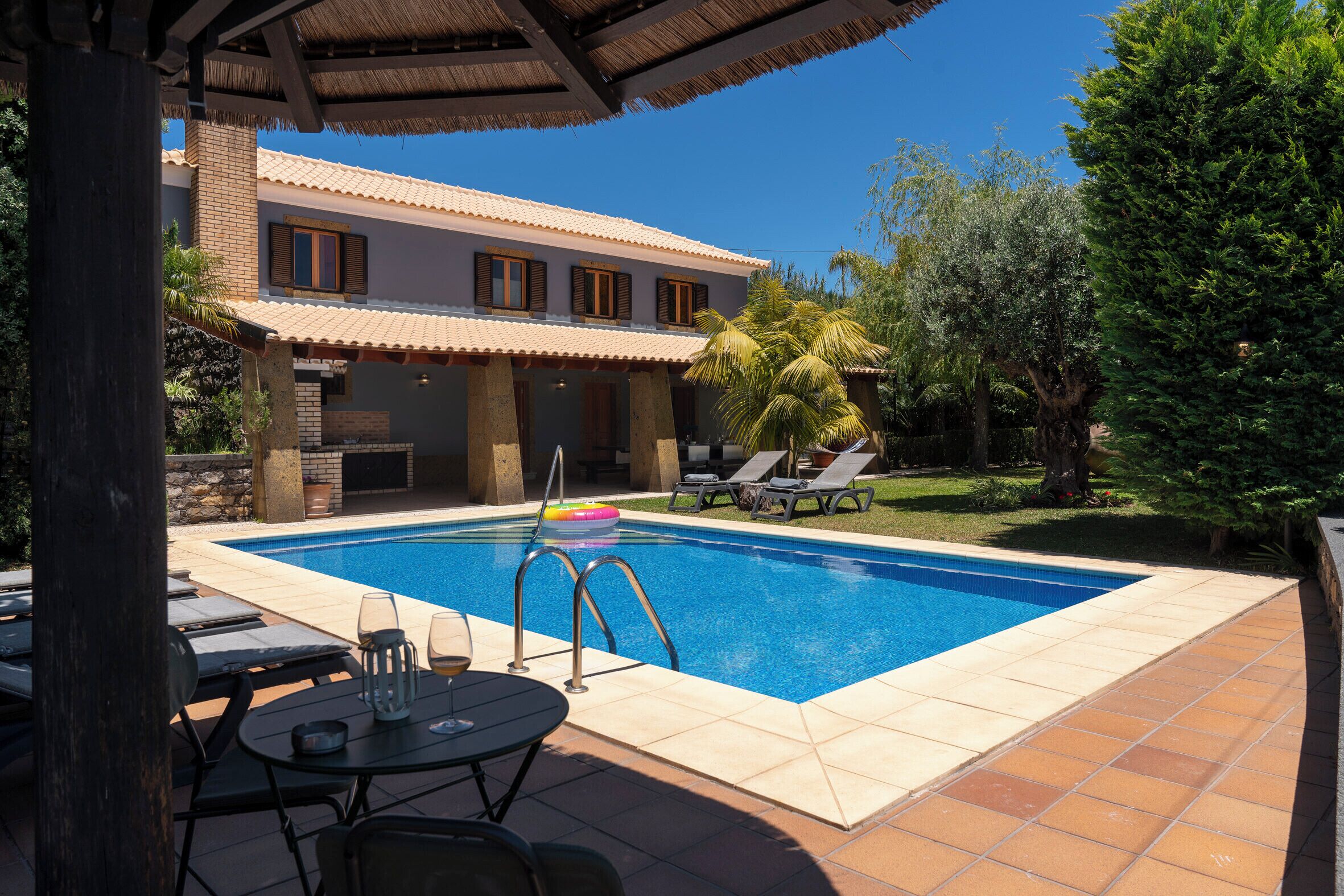Une piscine avec une terrasse carrelée, des chaises longues et un patio couvert.