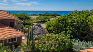 Um imóvel à beira-mar com estrutura de telhado de palha, um caminho que leva à praia e vegetação exuberante.