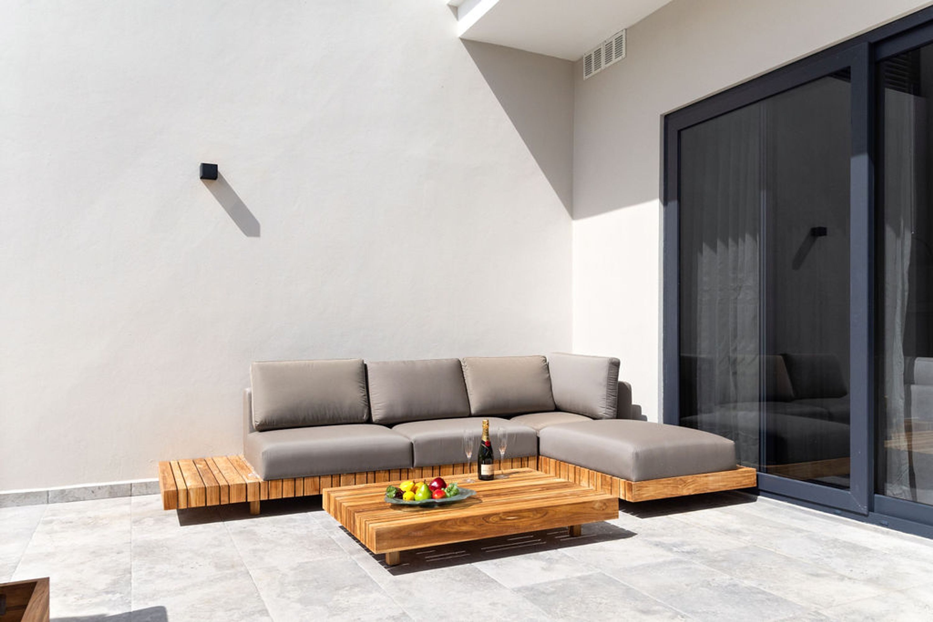 Un espace extérieur moderne, aménagé avec une table basse en bois, un canapé gris et une porte en verre.