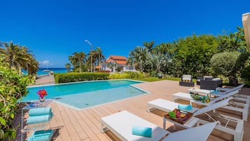 Zona junto a la piscina con sillones de descanso, piscina y vista al océano.