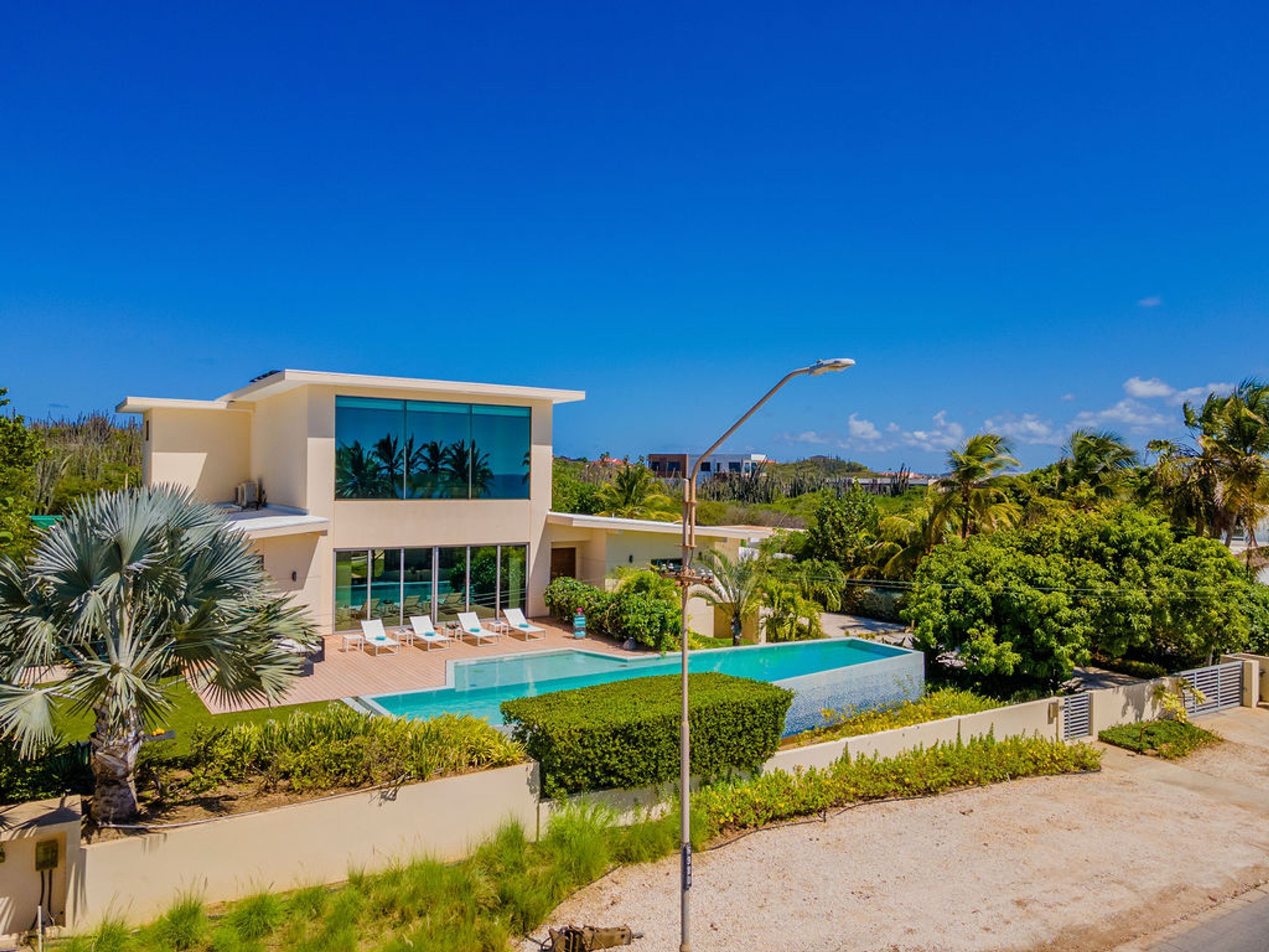 Une maison moderne à deux étages avec une piscine, entourée d’une végétation luxuriante et de palmiers.
