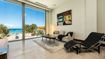 Un salón amplio con un gran ventanal con vistas a la playa, un sillón negro, un sofá color beige y una mesa de centro.