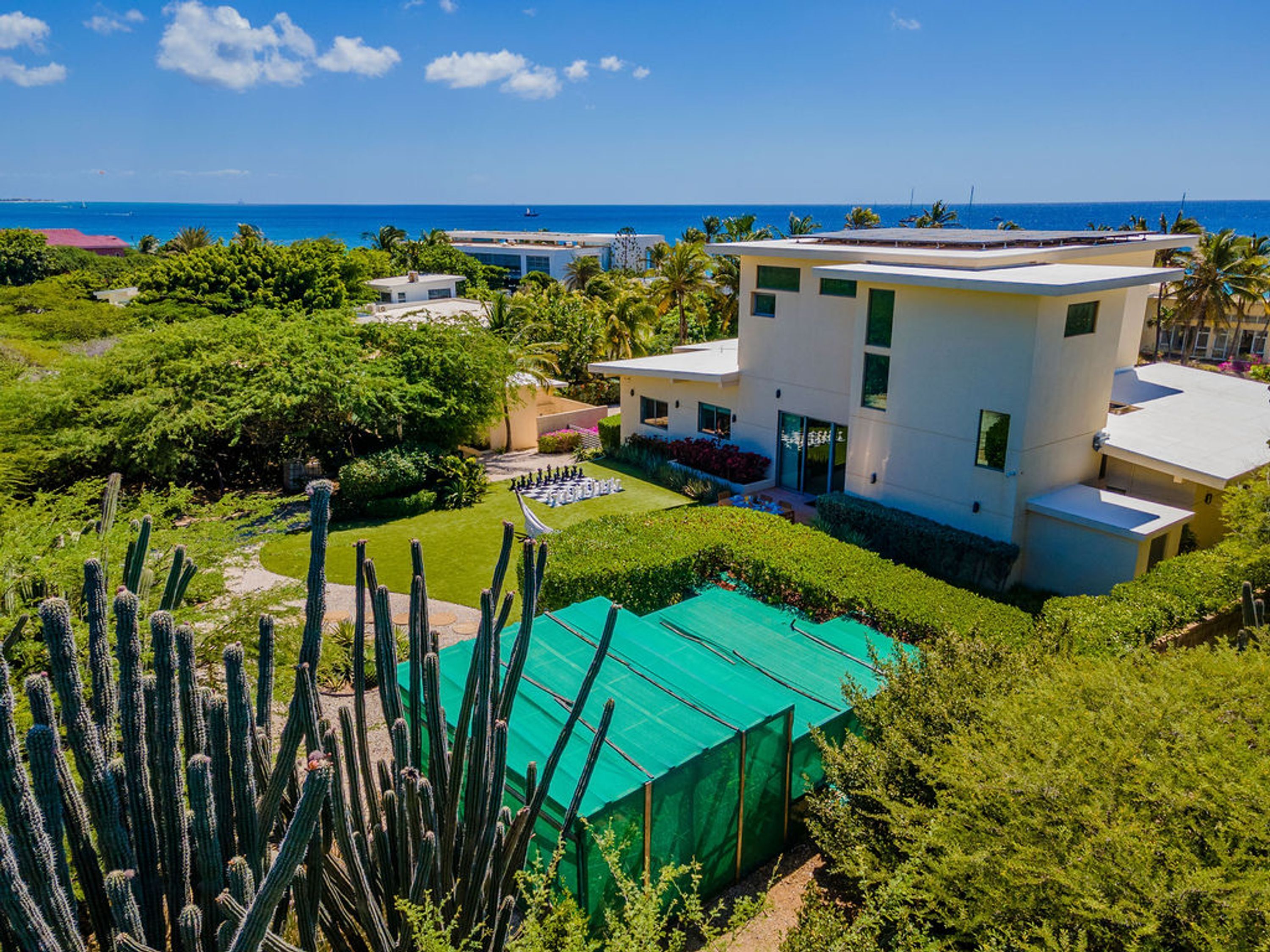 Uma casa moderna de dois andares com um jardim bem cuidado, uma estufa com telhado verde e vista para o oceano.