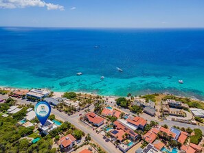 An aerial view of a coastal area with clear blue waters, boats, and a mix of residential and commercial buildings.