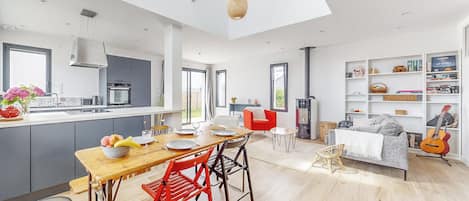 A modern kitchen with a dining area, a living room with a fireplace, and a bookshelf.