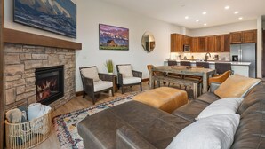 Een moderne woonkamer met een stenen open haard, een eethoek en een keuken met houten kastjes en roestvrijstalen apparatuur.
