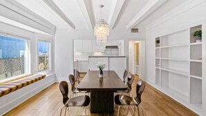 A modern dining room with a wooden table and chairs, a chandelier, and a view of the outdoors through large windows. - Long Beach Condo Home -Minutes Walk To The Beach (Long Beach)