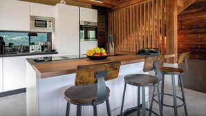 A modern kitchen with a wooden ceiling, white cabinets, a built-in microwave, and a large island with a fruit bowl and bar stools. - Chalet Emeraude des Alpes - peaceful break in the mountains - OVO Network (Saint-Pierre-d'Entremont)
