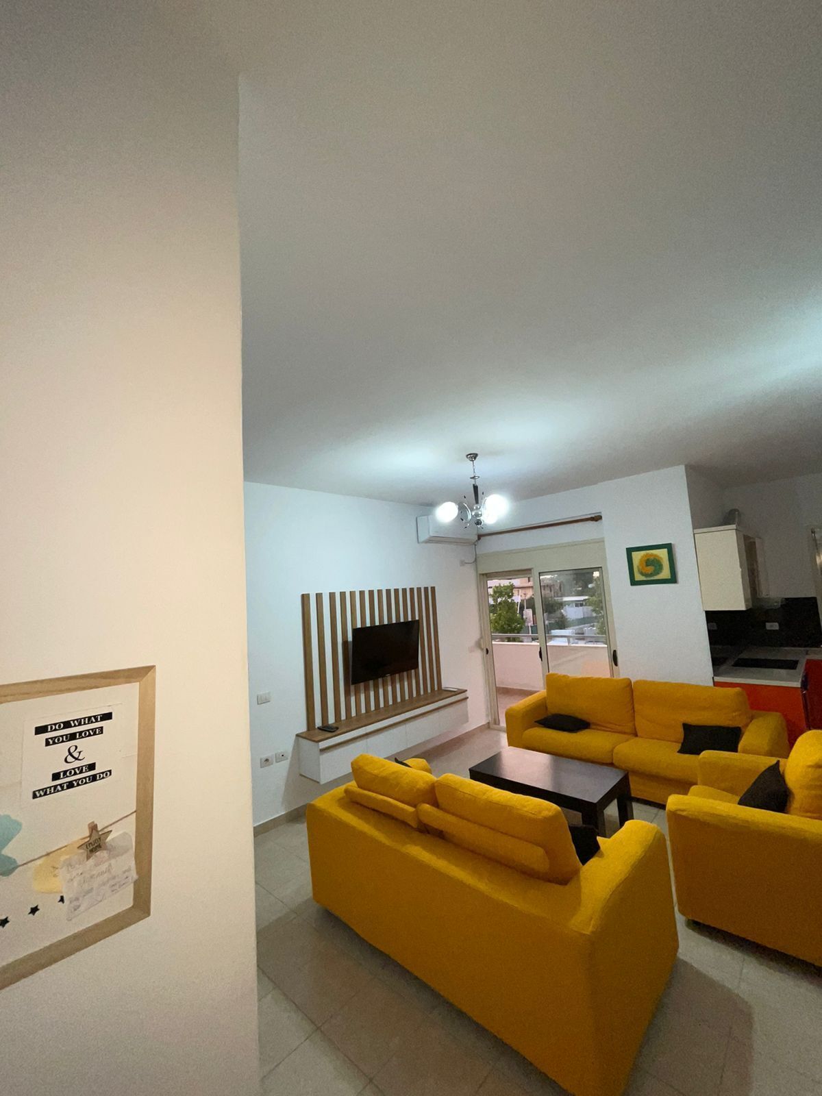 Olohuoneessa on keltaiset sohvat, seinälle asennettu taulutelevisio ja kattotuuletin.
