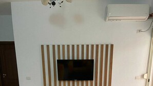 Un soggiorno con una TV a schermo piatto montata su una parete rivestita in legno, due divani gialli con cuscini neri e un tavolino da caffè nero.