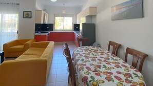 Un ambiente compatto con tavolo da pranzo, divano giallo e angolo cottura.
