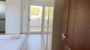 Una camera d'albergo con un letto, una porta di legno e vista sul balcone esterno.