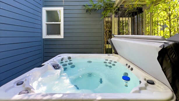 A hot tub with a window above it, surrounded by a dark blue house wall.