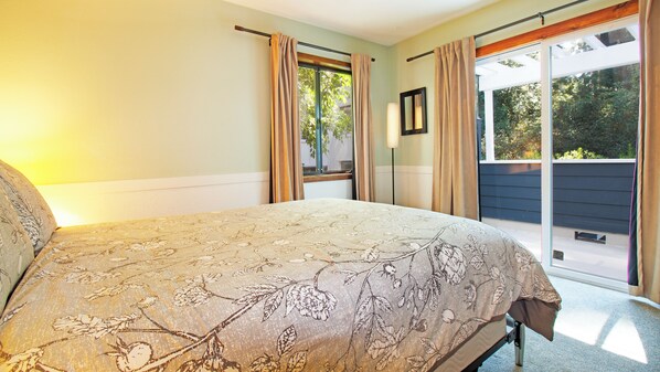 A bedroom with a bed, a window with curtains, and a view of greenery outside.