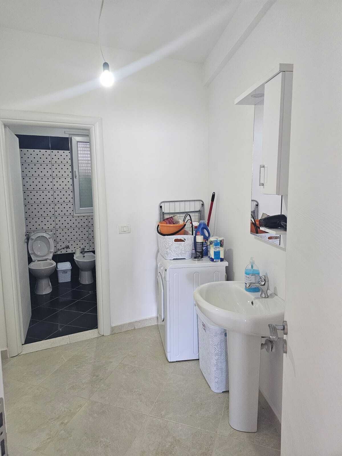 A small, clean bathroom with a sink, mirror, and two toilets.