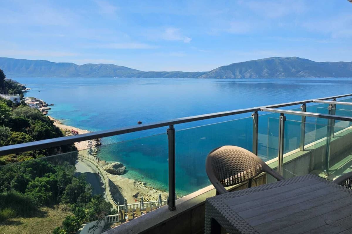 A balcony with a clear view of a coastal landscape, including a beach and mountains.