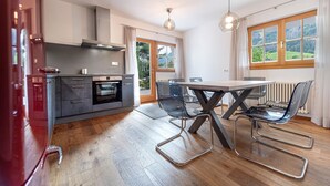 A modern kitchen with a dining area, featuring a wooden floor, a table with chairs, and a view of the outdoors through a window. - 175A Panoramic Apartment 24 (Ortisei)