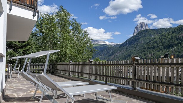 A balcony with sun loungers, a stone floor, and a view of mountains. - 175A Panoramic Apartment 24 (Ortisei)