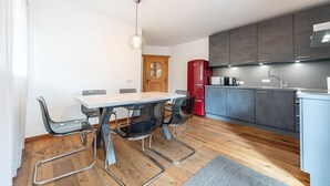 A modern kitchen with grey cabinets, a red refrigerator, and a wooden dining table with metal chairs. - 175A Panoramic Apartment 24 (Ortisei)
