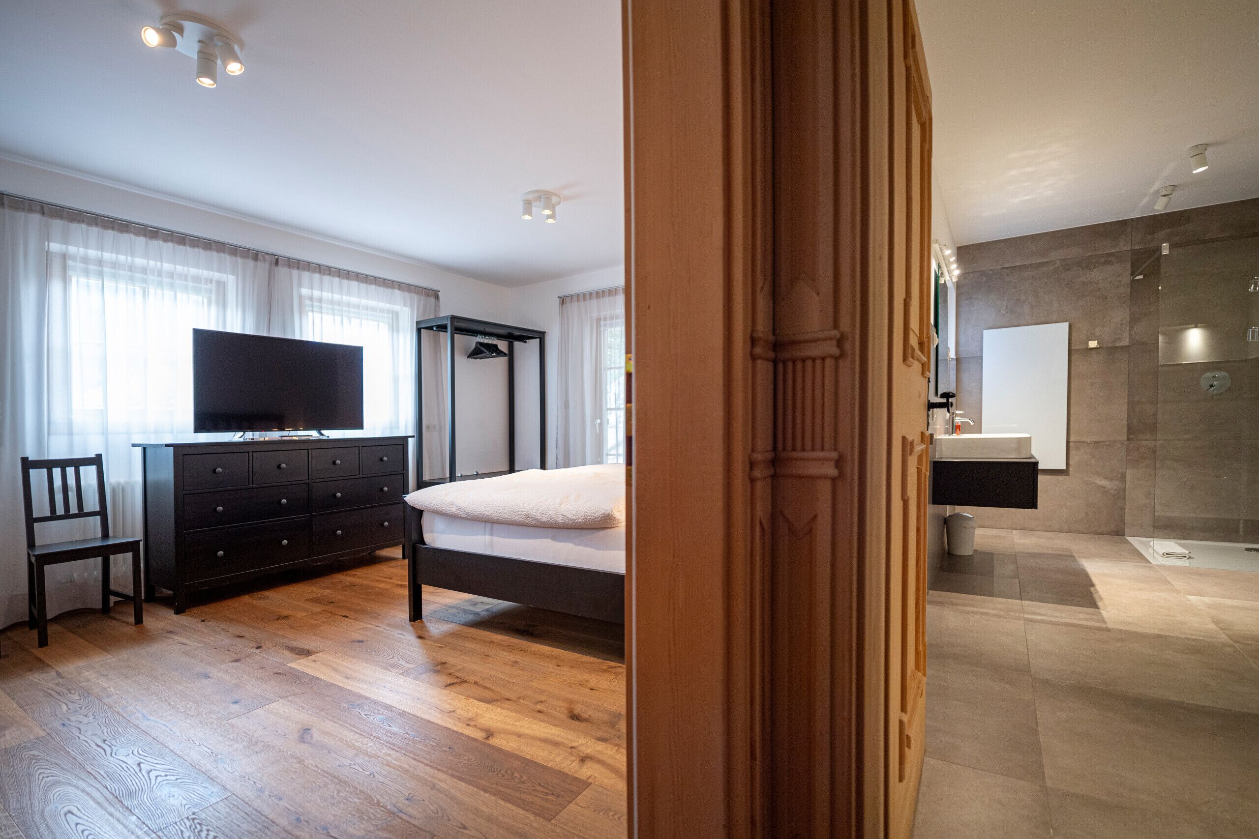 Ein Schlafzimmer mit Bett, Kommode, Fernseher und Holzboden.