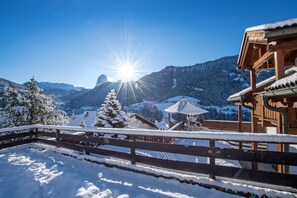 Un chalet en bois, avec un toit enneigé, une clôture en bois et une vue sur les montagnes en arrière-plan.