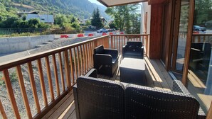 A balcony with wicker furniture, a view of a road, and distant buildings.