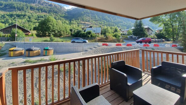 A balcony with wicker furniture, a view of a road with cars, and houses in the background.