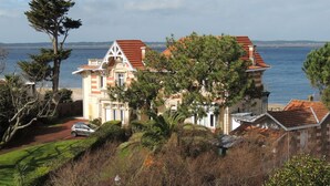 Un edificio costero con techo de tejas rojas, rodeado de vegetación y vistas al mar.