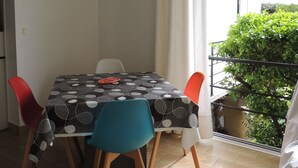 Un comedor con una mesa cubierta con mantel estampado, rodeada por cuatro sillas, una de ellas azul. Una lámpara colgante se suspende sobre la mesa.