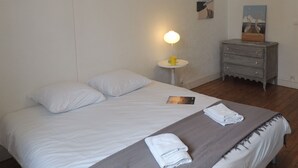 Una cama bien hecha con almohadas, una mesita de noche con lámpara, un tocador pequeño y un cuadro en la pared.