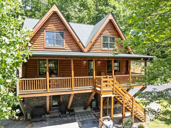 A log cabin with a balcony, a staircase, and a porch area. - Hot Tub, Fiber-optic WiFi, Pool Table, Playground, EV charger. Cozy Log Cabin. (Waynesville)