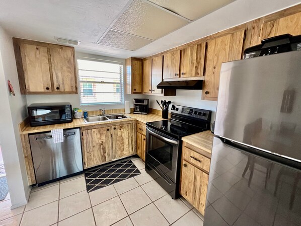 Una cocina moderna con gabinetes de madera, electrodomésticos de acero inoxidable, un microondas negro, una cafetera y un refrigerador.