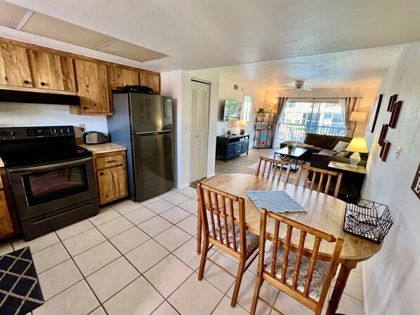 A compact kitchen with a refrigerator, oven, and wooden cabinets. There is a dining area with a table and chairs.