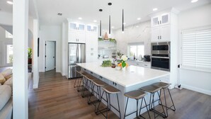 A modern kitchen with a large island, bar stools, stainless steel appliances, and white cabinetry.