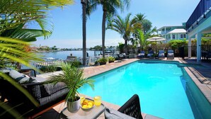 A pool area with lounge chairs, a table with drinks, and a view of the water.