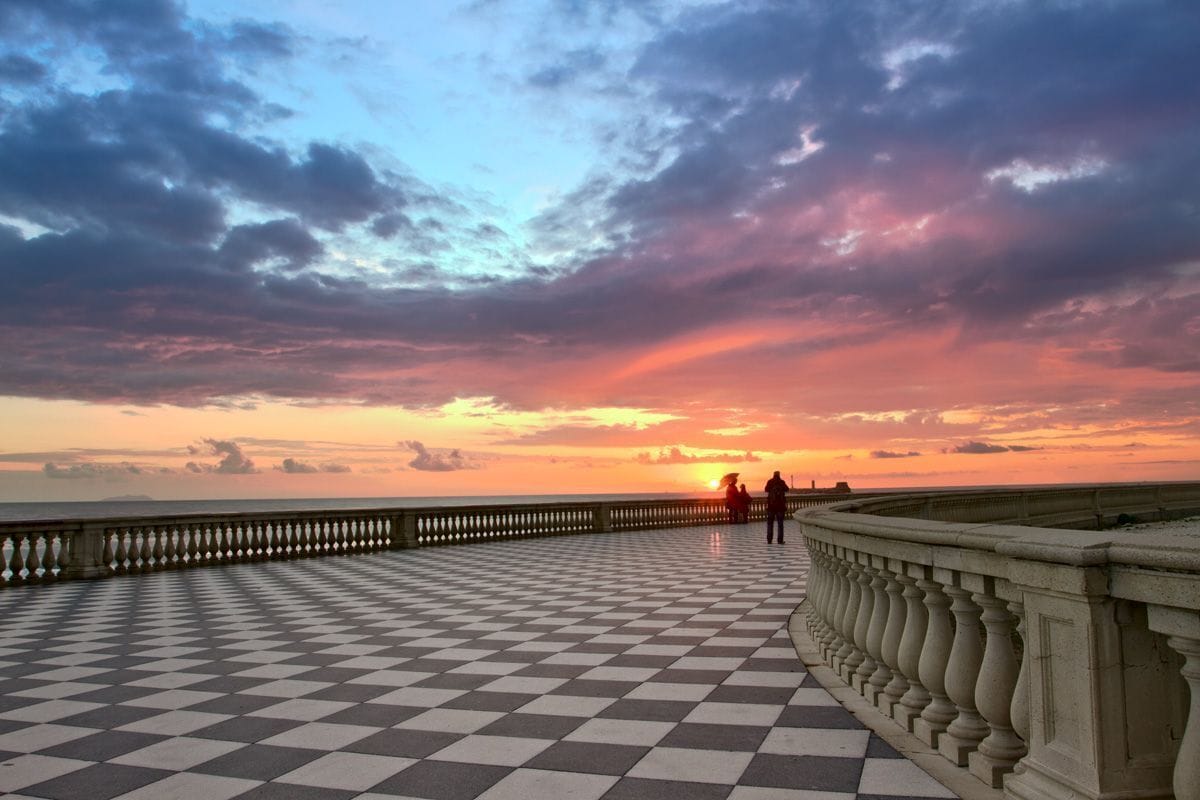 A checkered promenade with a balustrade and a sunset view.