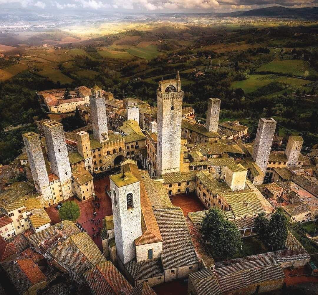 A medieval town with a prominent church featuring a tall bell tower, surrounded by smaller buildings and a hilly landscape in the background.